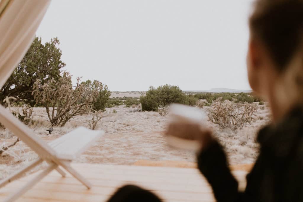 Girl Hold Drinks and Looks out at Desert View from Canvas Glamping Tent in Santa Fe New Mexico