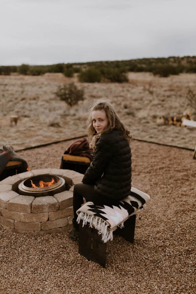 Girl Sits by Campfire with Desert Landscape in the Background in Santa Fe New Mexico