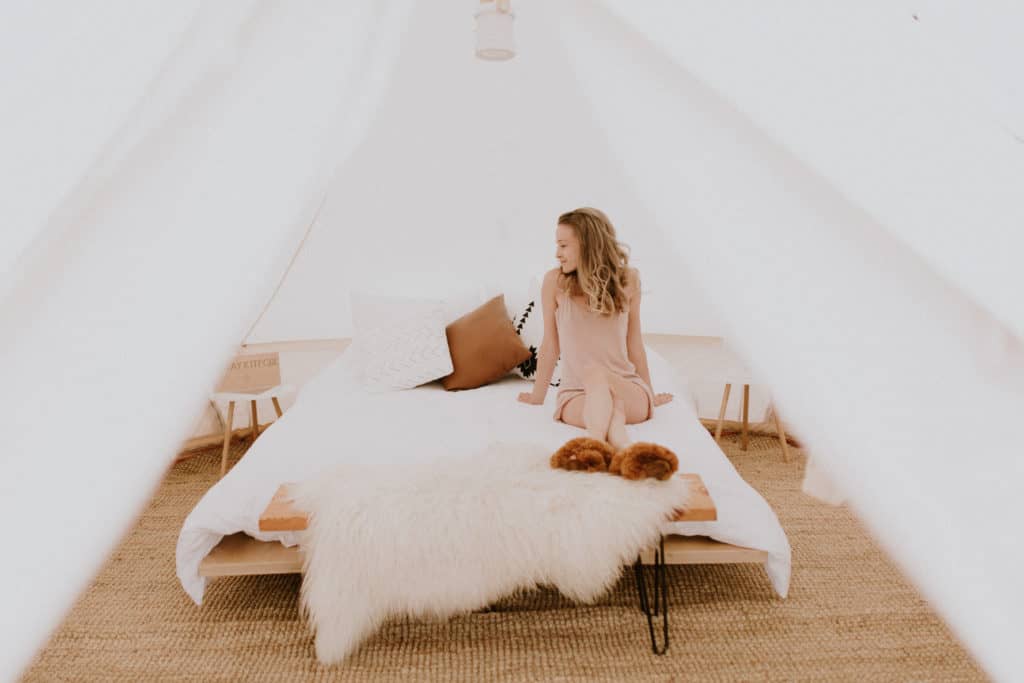 Girl on White Bed with Sheepskin and Brown Alpaca Fur Slippers with Southwest Style Bedding in a Canvas Tent at a Glamping Retreat in New Mexico