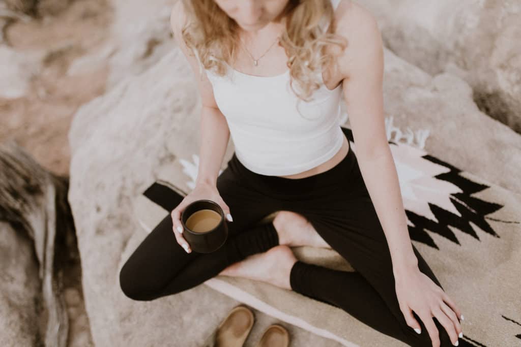 Girl with Black Leggings Sits Pretzel Legged on Southwestern Blanket Holding Coffee